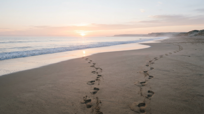 Two sets of footprints heading in different directions along a quiet beach at sunrise.